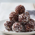 Healthy no-bake chocolate protein balls stacked on a plate with oats and cocoa.